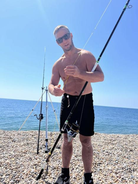 Man preparing fishing rod on a pebbly beach.