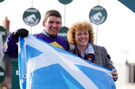 Jockey Derek Fox and trainer Lucinda Russell holding a Scottish flag after a race win.