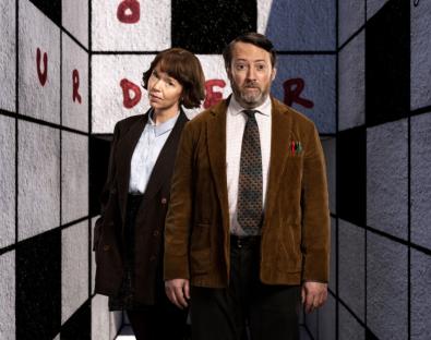 Promotional image of two people standing in a crossword puzzle-themed room.