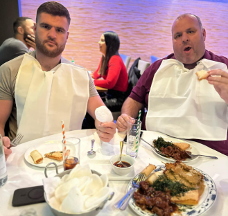 Two men wearing bibs at a restaurant table eating Chinese food.