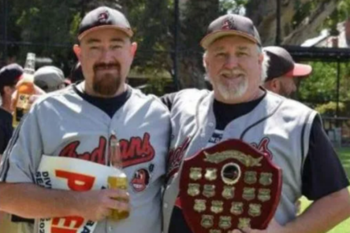 Two men in baseball uniforms holding a trophy.