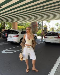 Woman in white shorts and beige top standing in a hotel parking lot.