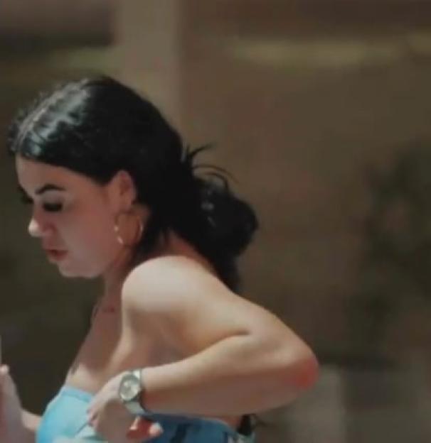 A woman in a light blue strapless top with dark hair pulled back and gold hoop earrings.