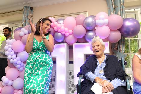 A woman applauds as a 115-year-old woman sits in a wheelchair in front of a