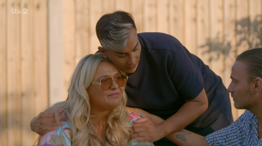 Screenshot of a woman being comforted by a person while another person looks on.