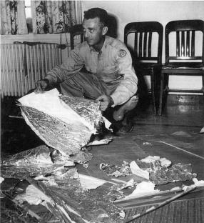Black and white photo of Jesse Marcel examining debris from a crashed weather balloon in Roswell, New Mexico.