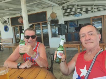 Two men sitting at an outdoor table, each holding a beer bottle.