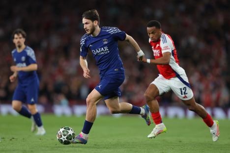 Khvicha Kvaratskhelia of Paris Saint-Germain dribbling the ball past an Arsenal player.