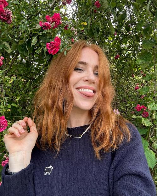 Angela Scanlon sticking out her tongue with a background of pink flowers.