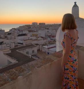 Woman in floral dress overlooking a city at sunset.
