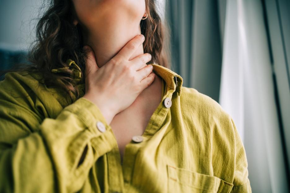 A woman holding her neck, suffering from a sore throat.