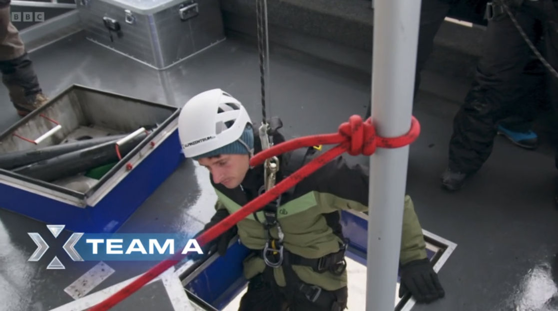 Person in safety gear descending into a hatch on a boat.