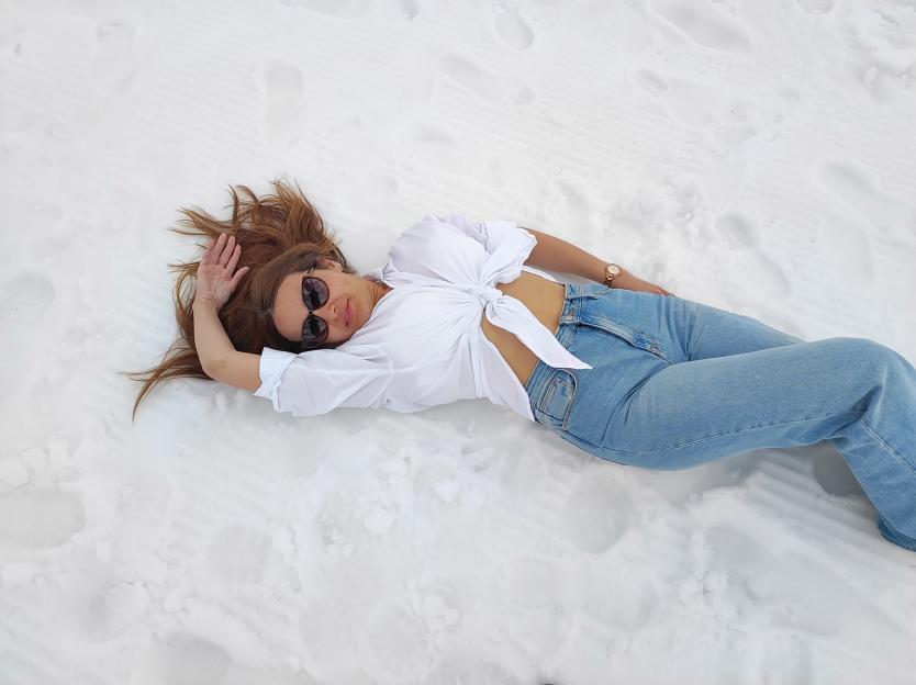 A woman in jeans and a white shirt lies on white sand.