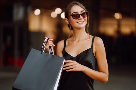 Woman in black dress holding shopping bags.