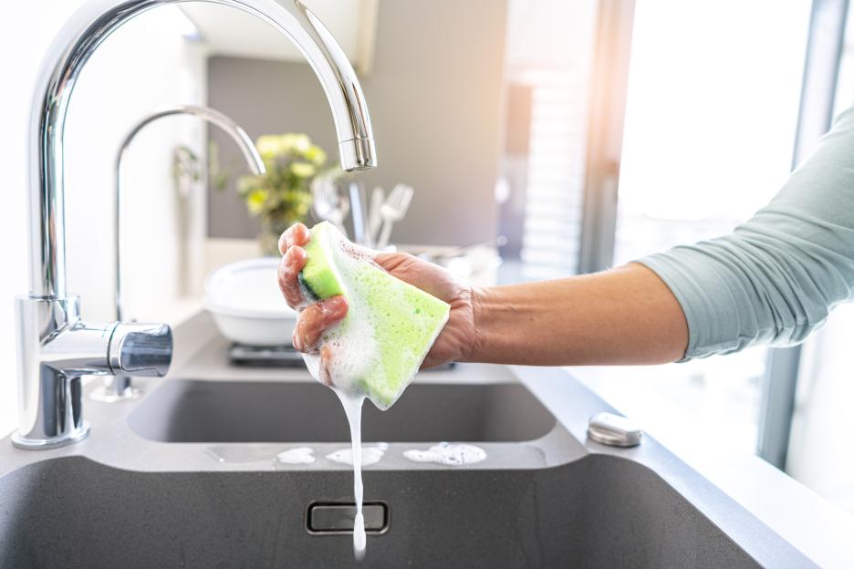 A hand rinsing a soapy sponge in a kitchen sink.