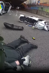 A person lying on the ground near a wrecked scooter and a police car.
