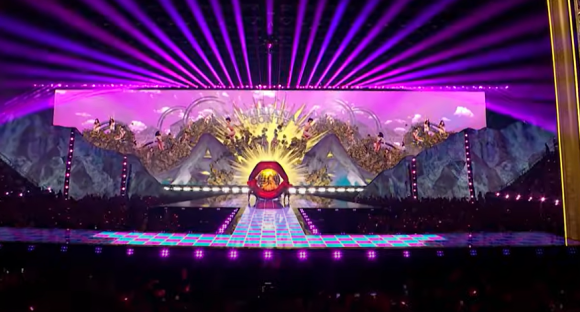 Concert stage with large video screen showing surreal landscape and giant lips.