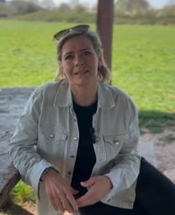 Woman sitting outdoors, speaking.