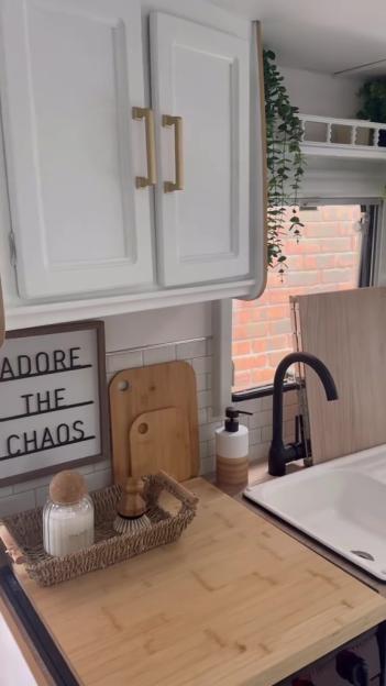 Kitchenette with white cabinets, light wood counters, a black faucet, and a small sign that reads "ADORE THE CHAOS."