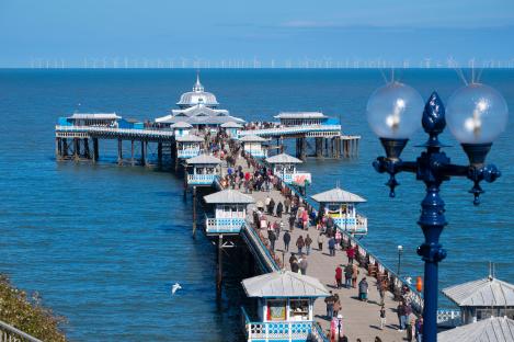 Llandudno pier with many people walking on it, and an offshore wind farm in the background.