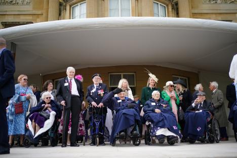 Veterans in wheelchairs and standing at Buckingham Palace watching a military flypast.