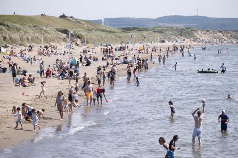 Crowded beach with people swimming and sunbathing.