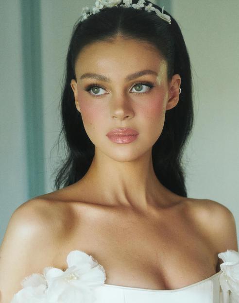 Portrait of Nicola Peltz Beckham wearing a flower crown and off-the-shoulder dress.
