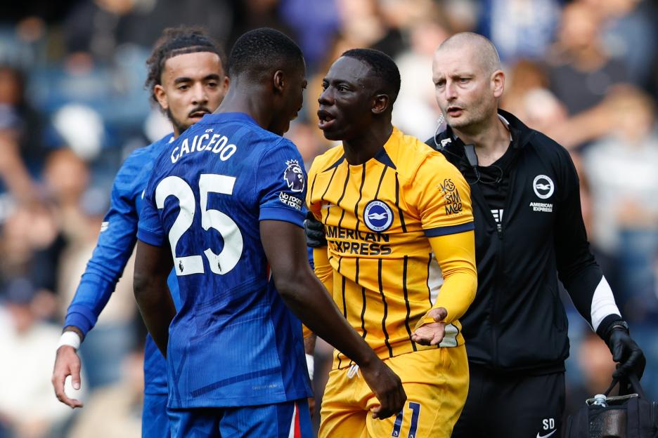 Moises Caicedo of Chelsea and Yankuba Minteh of Brighton clash during an English Premier League soccer match, with a staff member standing behind Minteh.
