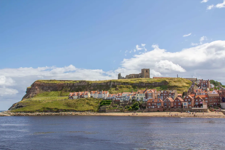 Houses and Whitby Abbey on a cliff overlooking a beach.