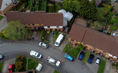 Aerial view of a residential street with parked cars and emergency vehicles.