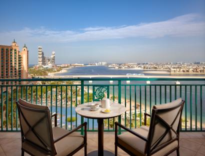 Balcony view of ocean and city skyline with two chairs and a table.