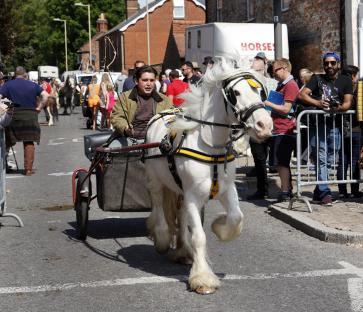 A white horse pulling a cart down a street at a horse fair.
