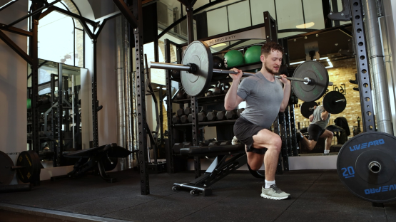 Man performing a barbell split squat in a gym.