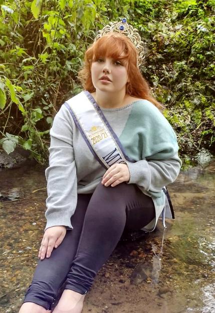 Megan Byrne, Miss Voluptuous Wales, sitting in a shallow stream with a tiara and sash.