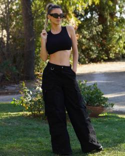 a woman in a crop top and wide leg pants stands in the grass