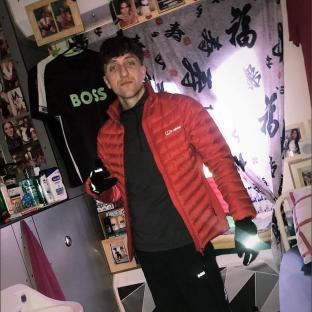 A man in a red jacket stands in a prison cell decorated with photos.