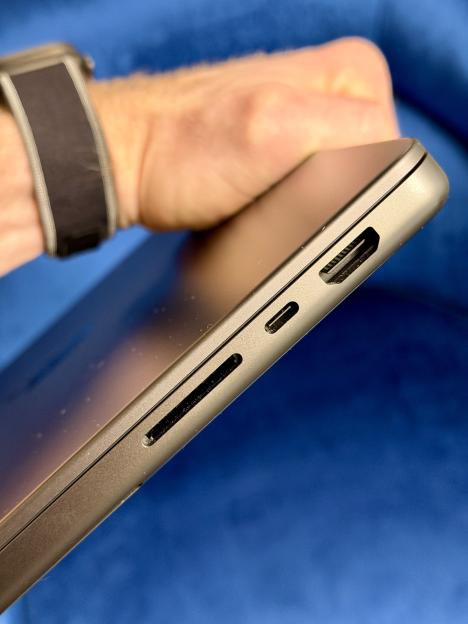 Side view of a MacBook Pro with USB-C and HDMI ports, with a hand visible in the background.