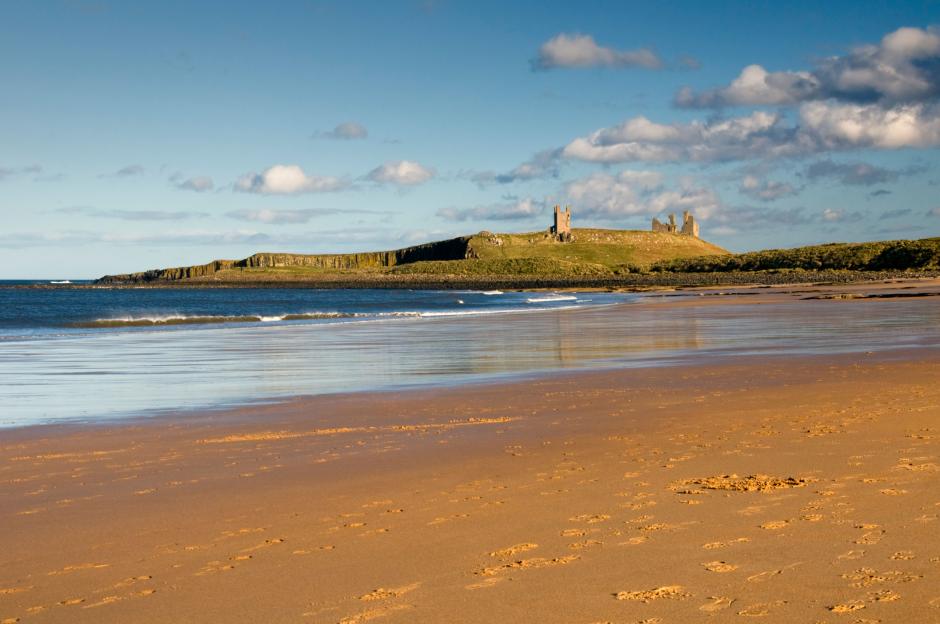 Dunstanburgh Castle ruins viewed from a sandy beach.