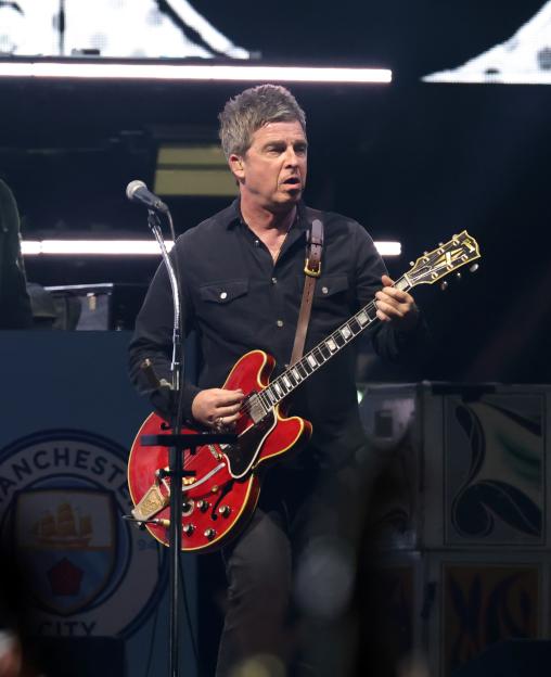 Noel Gallagher of Oasis performing onstage with a red Gibson guitar.