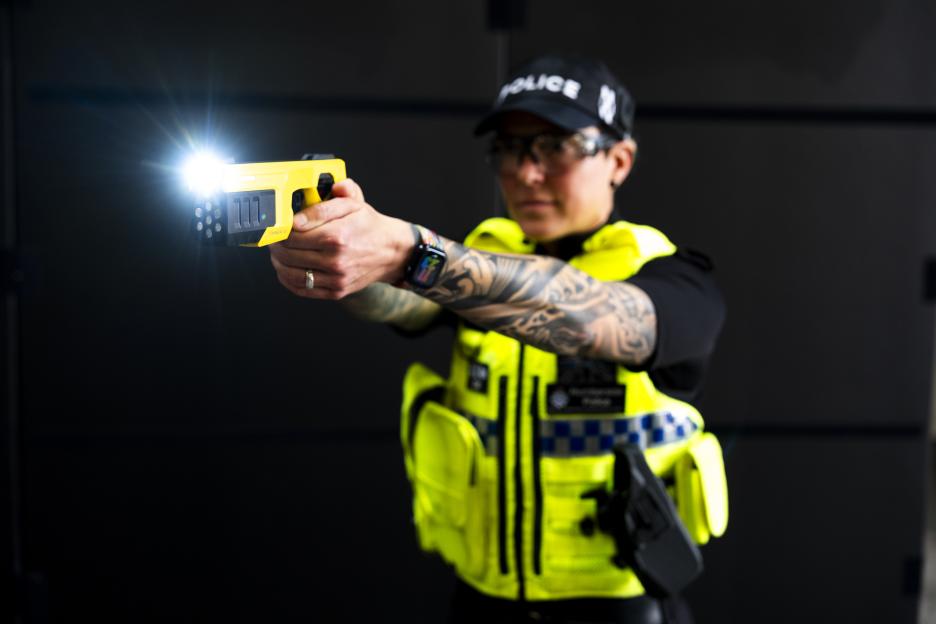 A firearms officer showcases the 'Taser 10' with a bright light emitted from the device.