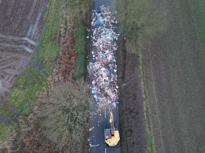 Aerial view of a construction vehicle removing a large pile of illegally dumped waste from a road.
