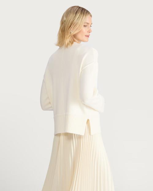 Woman wearing a cream-colored knit sweater and pleated skirt.