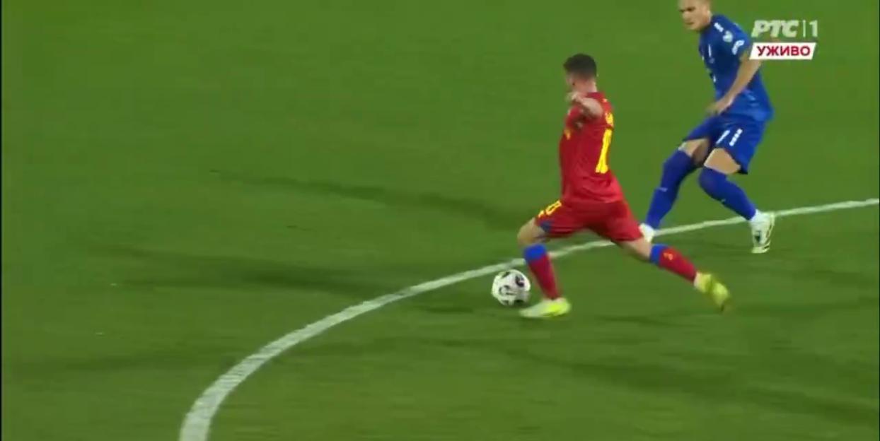 Two football players on a field with one in red kicking the ball and another in blue approaching him.