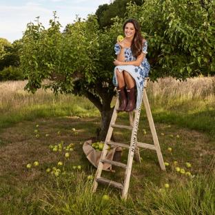 Woman sitting on a ladder under an apple tree, eating an apple.
