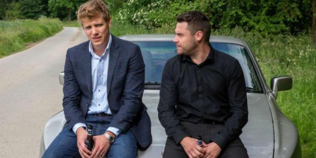 Aaron Dingle and Robert Sugden sitting on a car.