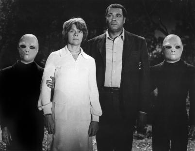 Still from *The UFO Incident*, showing Estelle Parsons and James Earl Jones flanked by two actors in alien masks.