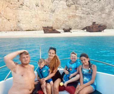 Family on a boat trip in Zante, Greece, with shipwrecks visible in the background.