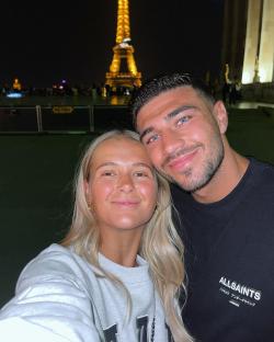 Couple posing for a selfie in front of the Eiffel Tower at night.