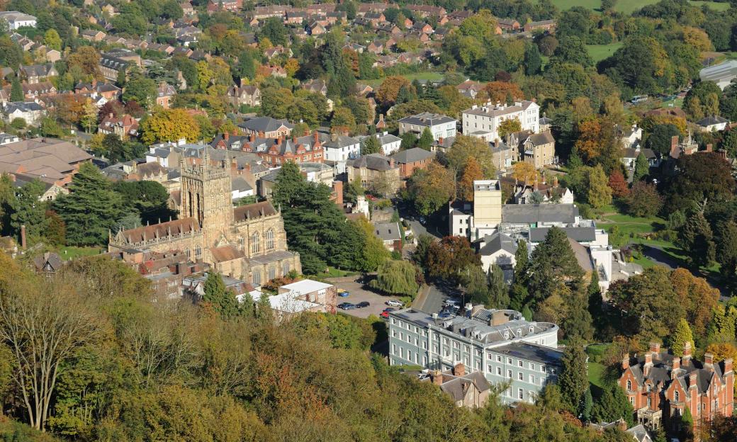 Aerial view of a town with a large stone church, houses with red roofs, and abundant green trees with some autumn colors.
