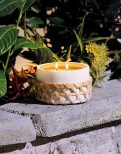 A lit citronella candle in a woven basket, sitting on a stone wall.